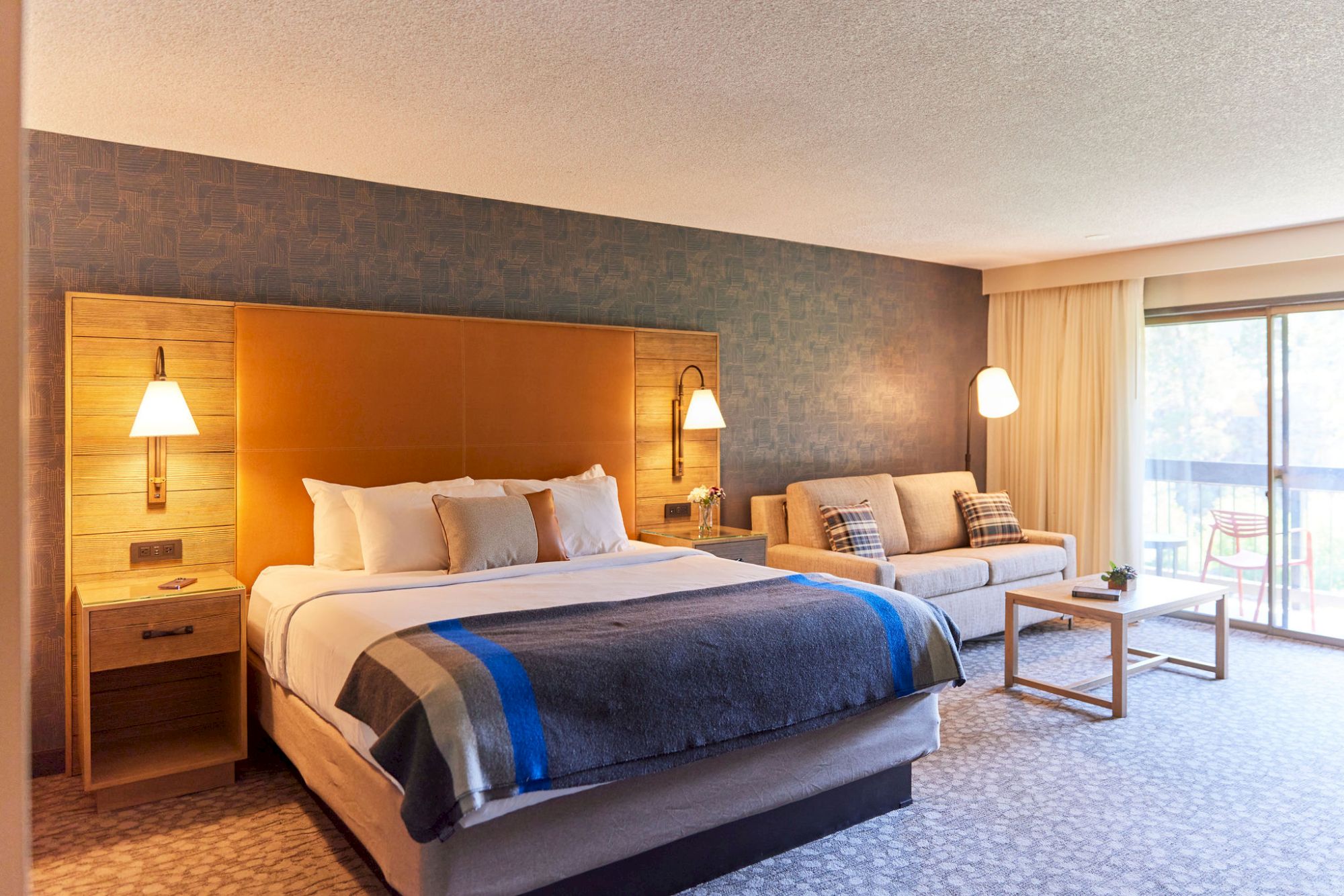 A modern hotel room with a King bed, lamps, seating area, and balcony access with views of Deschutes River in Bend, Oregon at Riverhouse
